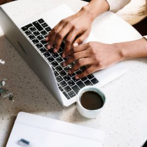 Laptop-open-on-desk-with-hands-coffee-cup-papers